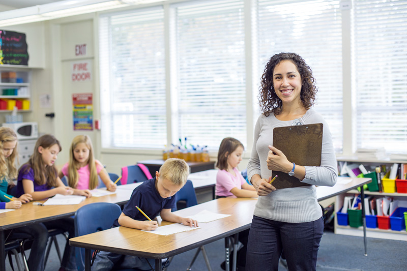 Female teacher smiling in classroom - focused teacher evaluation model concept