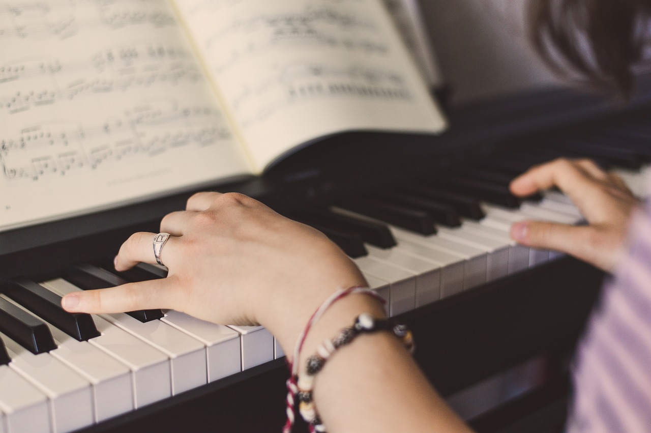 A close-up of hands playing a piano with sheet music open, illustrating the concept of deliberate practice.