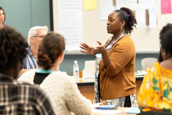 A female presenter leading a professional development session with a diverse group of educators.